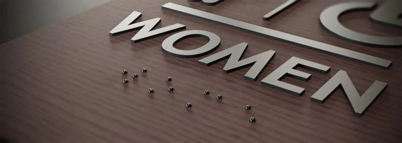 ADA room identification sign with tactile characters and Grade 2 braille in an apartment corridor